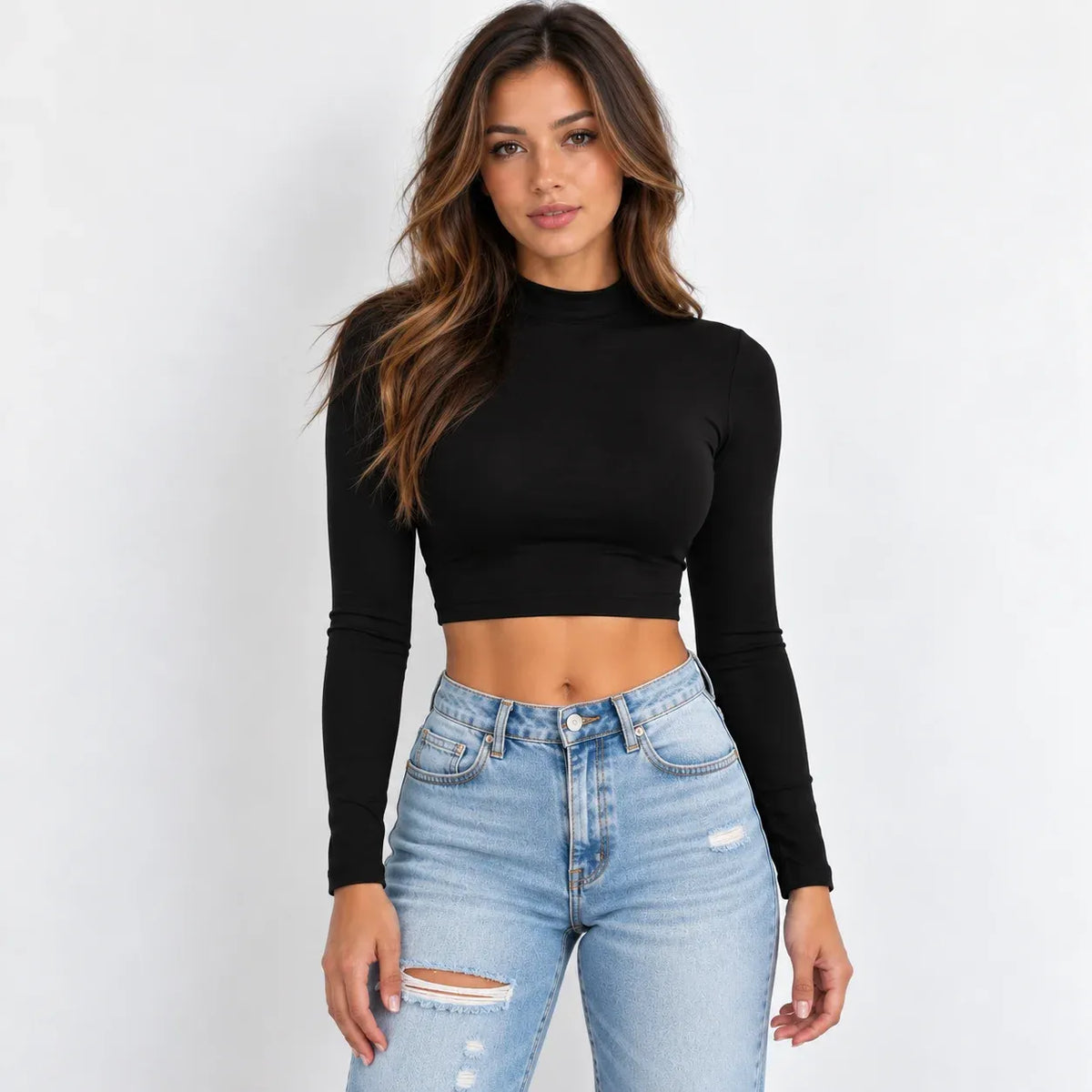A woman modeling a black long-sleeve mock neck crop top paired with light-wash distressed blue jeans against a plain white background.