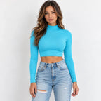 A woman modeling a light blue long-sleeve mock neck crop top paired with light-wash distressed blue jeans against a plain white background.