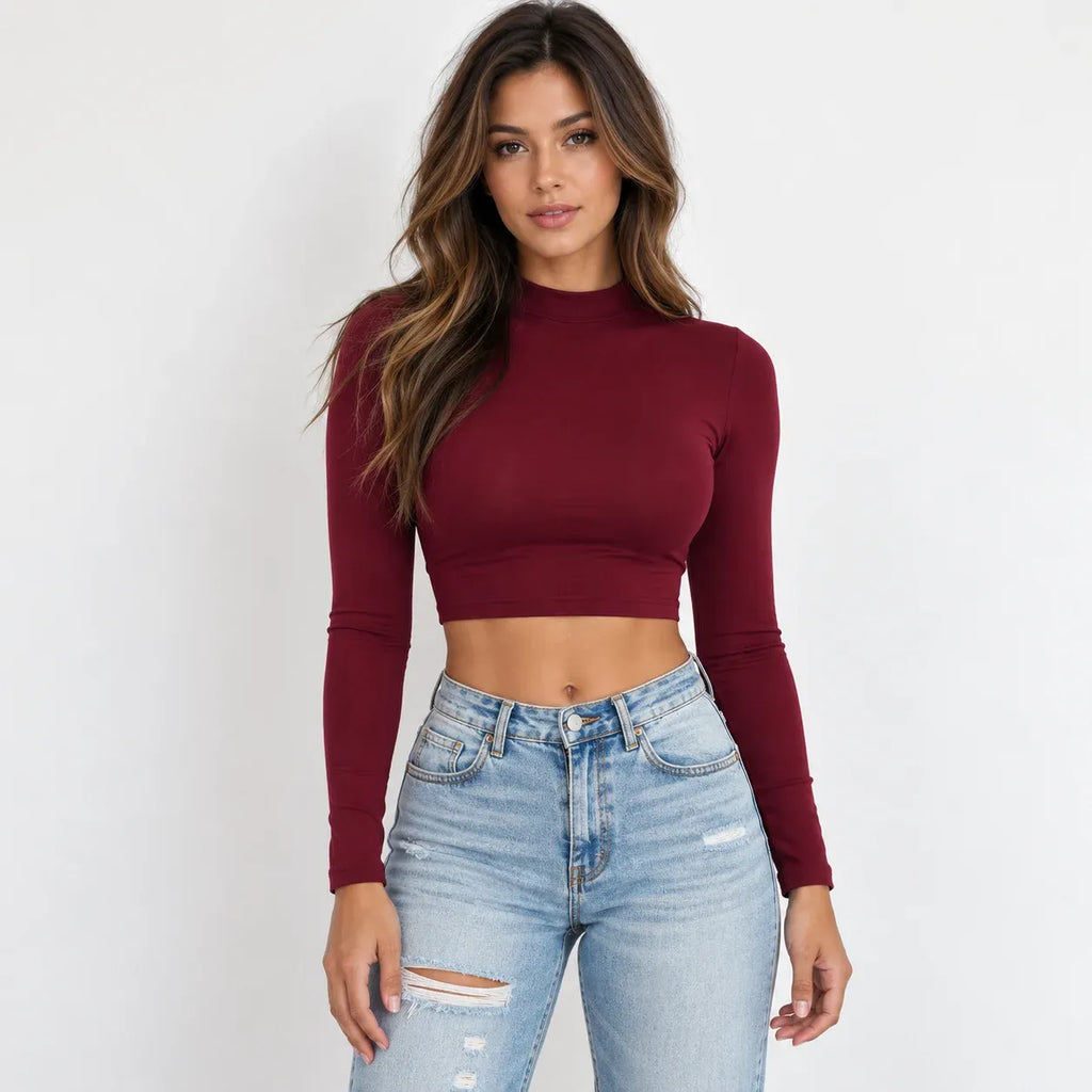 A woman modeling a wine red long-sleeve mock neck crop top paired with light-wash distressed blue jeans against a plain white background.