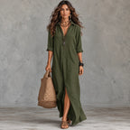 A woman models an olive green button-up maxi shirt dress with a high slit, holding a woven straw tote bag against a textured gray studio backdrop.