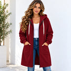 A woman wearing a long burgundy zip-up hoodie with a front pocket, white drawstrings, and a black inner collar, styled over a white tank top and blue jeans.