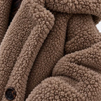 Khaki, close-up: Close-up of khaki teddy fleece coat showing the curled texture, lapel, sleeve, and dark front button.