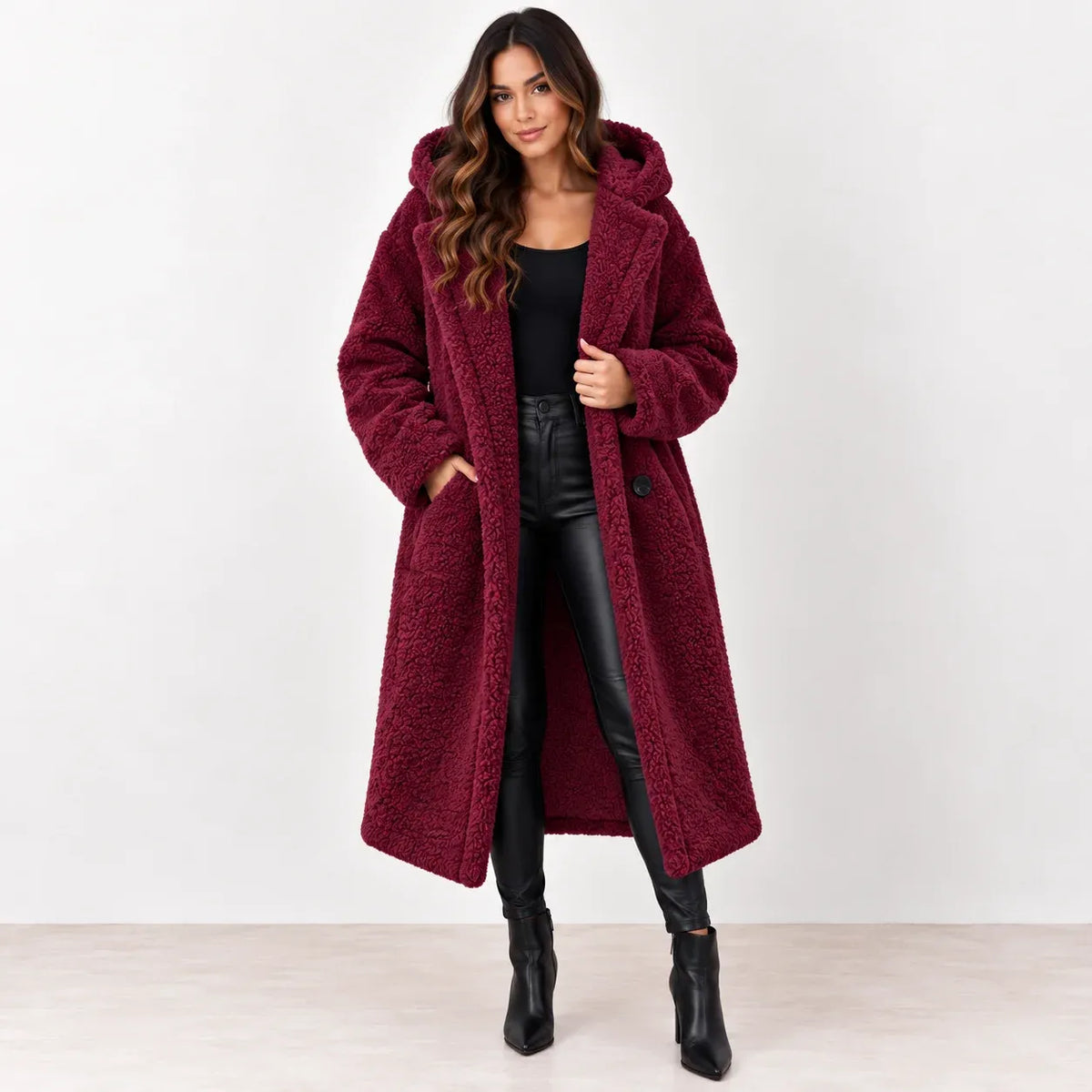 Wine red: Women's wine-red longline teddy fleece coat with hood and front pockets, styled over a black outfit.
