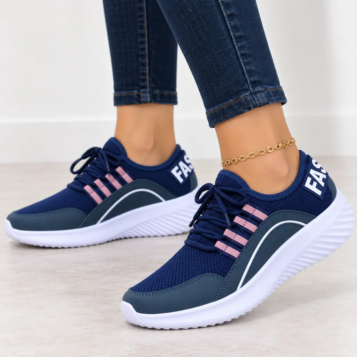 A pair of navy blue athletic sneakers with pink stripes and white soles, shown on a model wearing blue jeans. The shoes feature the partial white text 'FASE' on the side and heel.