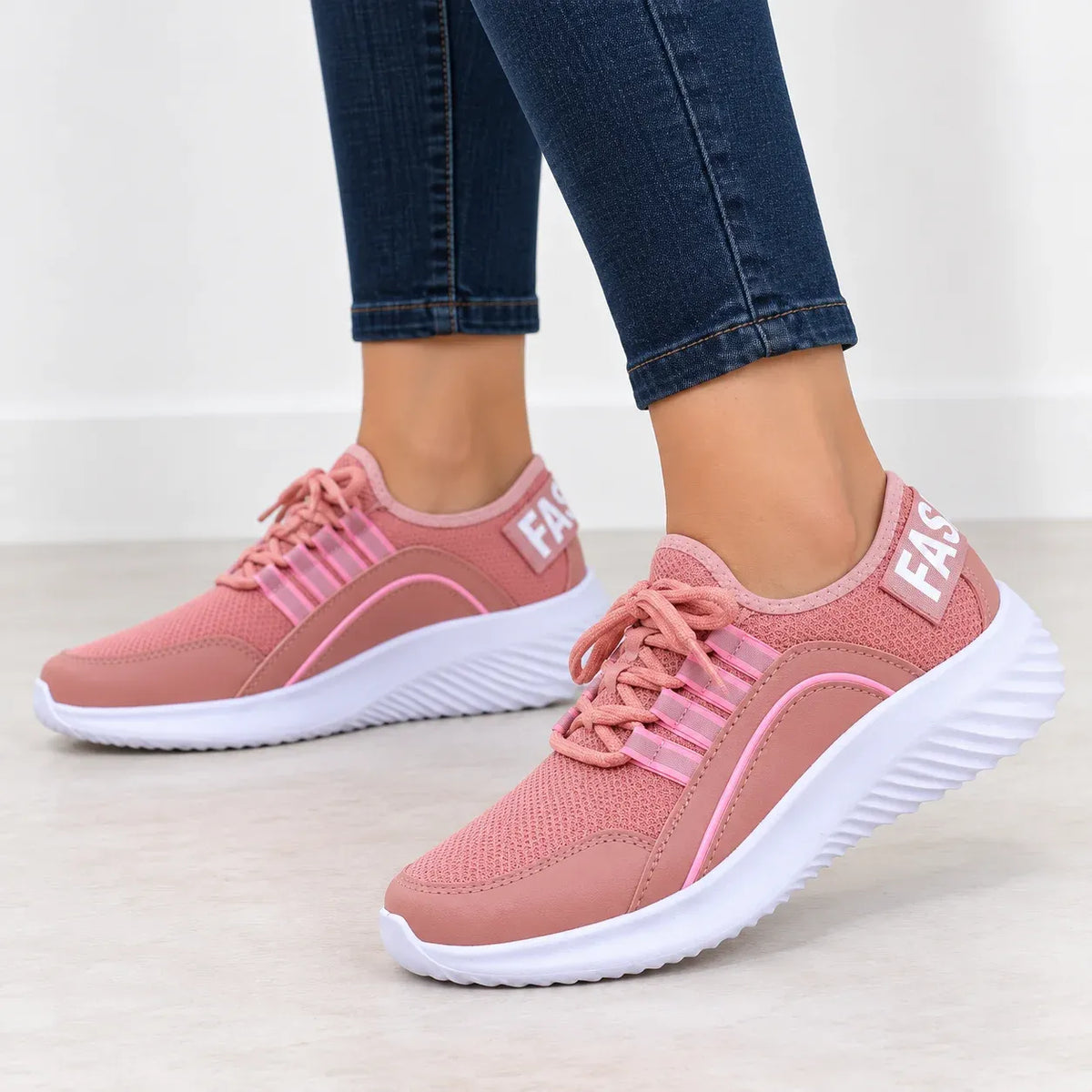 A pair of pink mesh sneakers with white soles, shown on a model wearing blue jeans. The shoes feature pink laces, pink stripe details, and a white heel tab with the brand name 'FASS'.