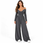 Charcoal front: Model wearing a charcoal grey off-shoulder wide-leg jumpsuit with slim straps and long sleeves.