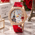 A women's rose gold watch with a red patterned leather strap, featuring a crystal-studded bezel and a dial decorated with the Eiffel Tower, hearts, and romantic script. The watch is displayed on a marble surface with Paris-themed decorative props, including a miniature Eiffel Tower figurine and a white 'PARIS' box.