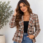A woman wearing a double-breasted plaid blazer in a rust orange, beige, and black pattern, styled with a black top and blue jeans against a light gray wall.