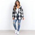 A woman modeling a black, white, and gray plaid hooded flannel shirt jacket over a white top and blue ripped jeans, standing against a plain white wall.
