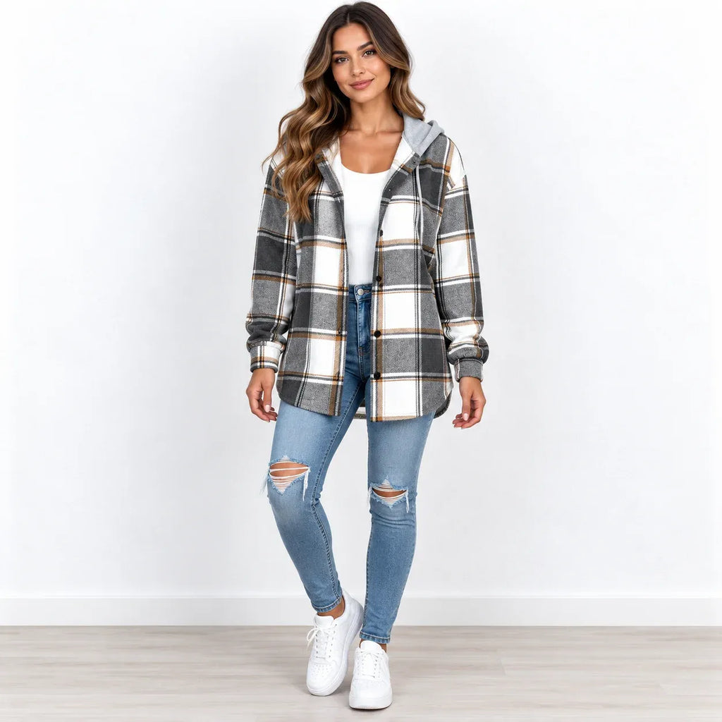 A woman modeling a gray, white, and black plaid hooded button-up shirt jacket, paired with a white top, distressed blue jeans, and white sneakers, set against a plain white wall and light wood floor.