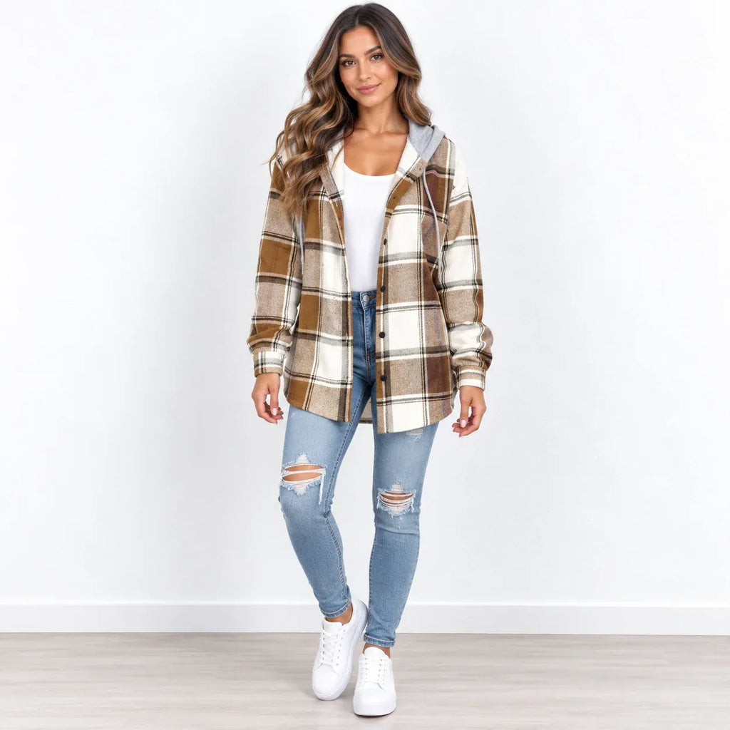 A woman modeling a brown and beige plaid hooded button-up shirt jacket over a white top, paired with light blue distressed jeans and white sneakers, standing against a white wall.