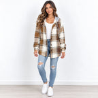 A woman modeling a brown and beige plaid hooded button-up shirt jacket over a white top, paired with light blue distressed jeans and white sneakers, standing against a white wall.