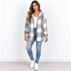 A woman modeling a gray and white plaid hooded button-up shirt jacket over a white top and distressed blue jeans, standing against a plain white wall.