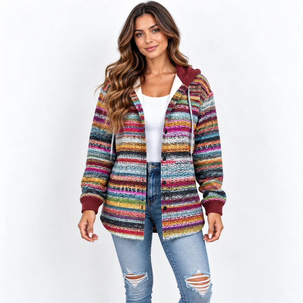 A woman modeling a colorful, striped knit zip-up hoodie with a hood and drawstrings, worn over a white tank top and blue jeans, against a plain white background.