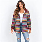 A woman modeling a colorful, striped knit zip-up hoodie with a hood and drawstrings, worn over a white tank top and blue jeans, against a plain white background.