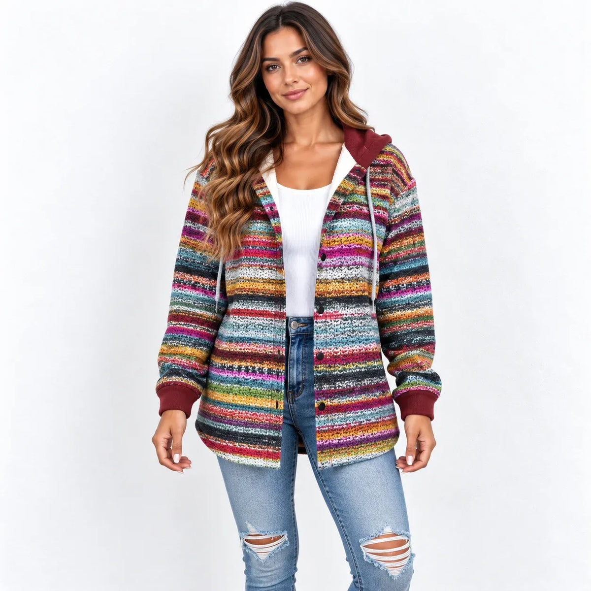 A woman modeling a colorful, striped knit zip-up hoodie with a hood and drawstrings, worn over a white tank top and blue jeans, against a plain white background.