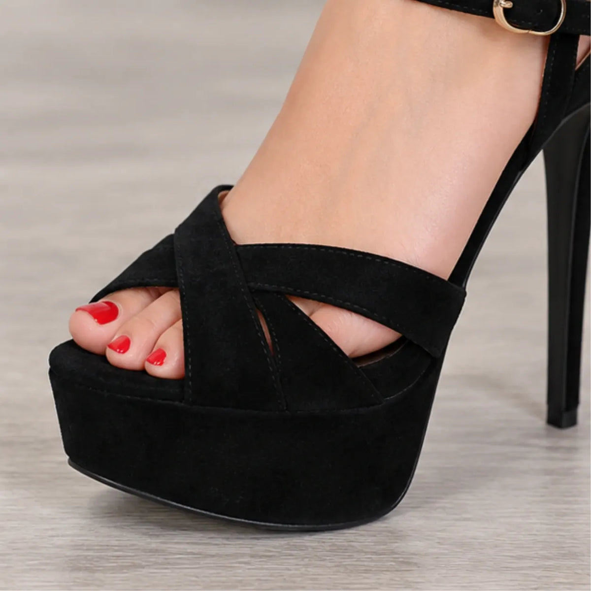 Black platform high-heeled sandals with crisscrossing ankle straps, shown on a model's foot against a light gray wood floor.