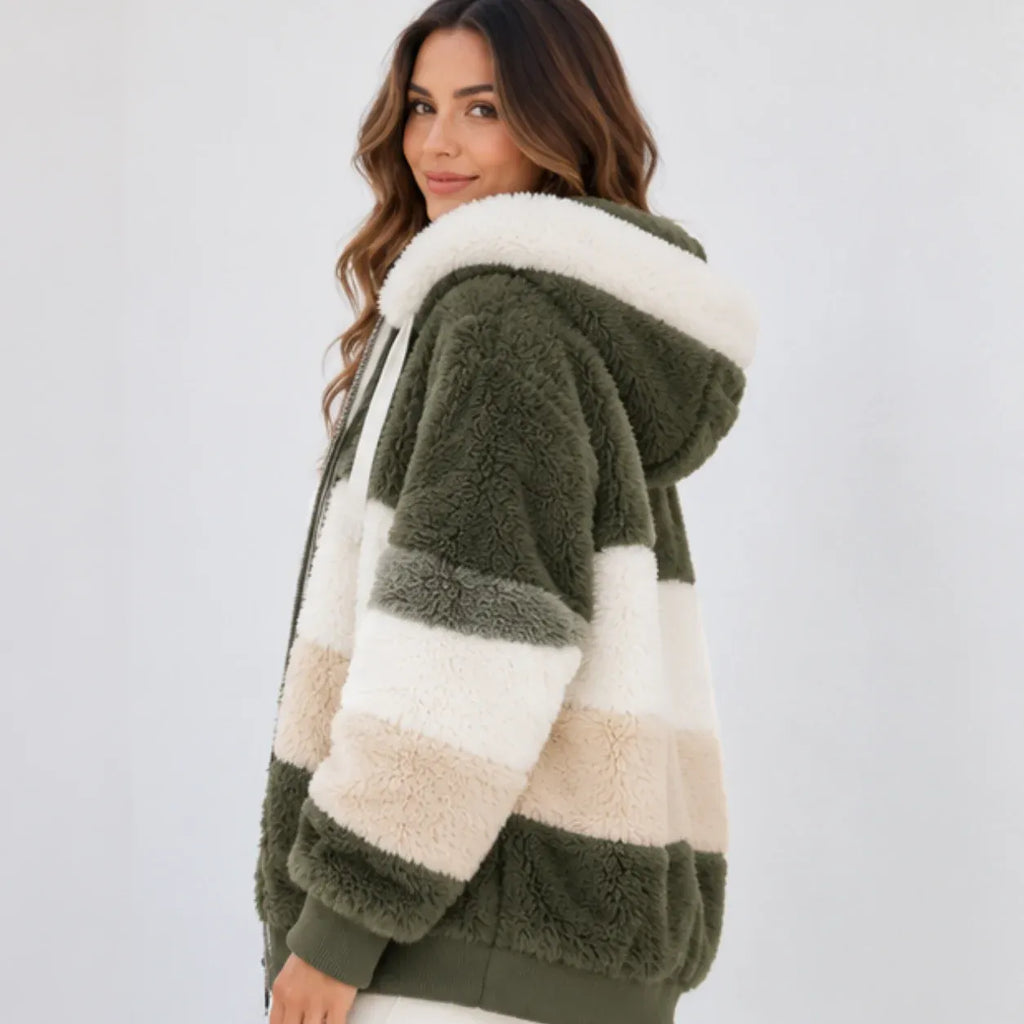 A woman wearing a plush sherpa hoodie jacket with horizontal stripes in olive green, cream, and light beige, photographed against a plain light gray studio background.