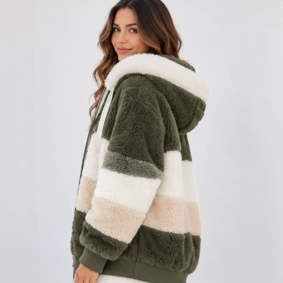 A woman wearing a plush sherpa hoodie jacket with horizontal stripes in olive green, cream, and light beige, photographed against a plain light gray studio background.