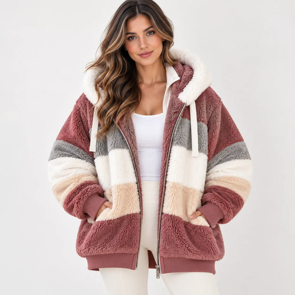 A woman wearing a plush sherpa zip-up hoodie jacket with horizontal stripes in dusty rose, cream, beige, and gray, styled over a white tank top and white pants against a light gray studio background.