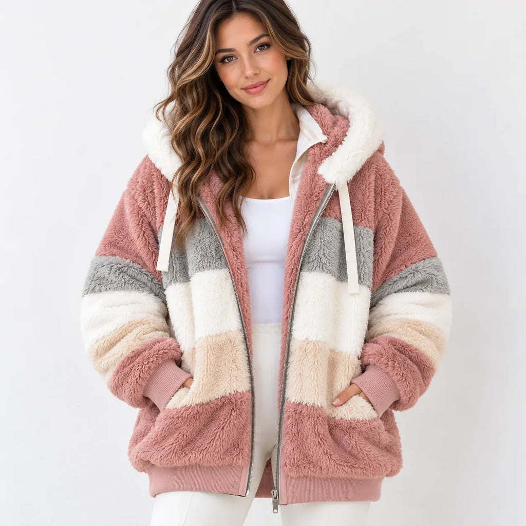 A woman wearing a fuzzy zip-up hoodie jacket with horizontal stripes in dusty pink, cream, beige, and light gray, paired with a white top and white pants against a light gray studio background.
