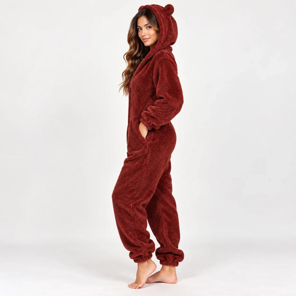 A woman modeling a plush, one-piece bear-themed pajama suit in a deep burgundy red color, standing against a plain white studio background.