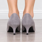 A pair of women's gray suede high-heeled pumps shown from the back, worn on a model's feet over a light wood floor.