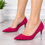 A pair of women's pointed-toe kitten heel pumps in a vibrant magenta pink suede, shown on a model's feet against a light gray wood floor and white wall background.