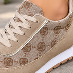 A close-up of a beige low-top sneaker with a woven monogram pattern, beige laces, and a white midsole, shown worn on a foot.