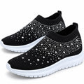 Black pair: Pair of black knit slip-on sneakers with rhinestone embellishments, ribbed openings, and white soles.