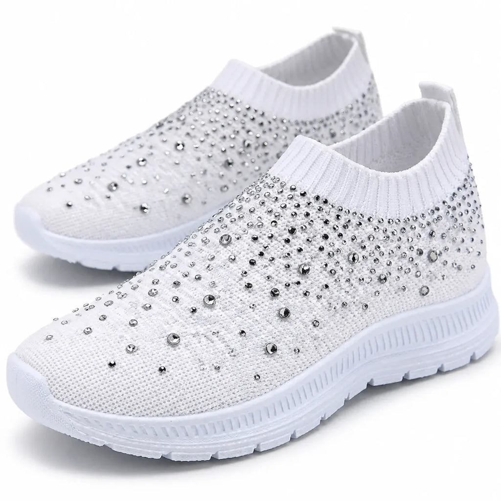 White close-up: Close-up of white knit slip-on sneakers showing rhinestone detailing, ribbed openings, and textured soles.