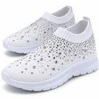 White close-up: Close-up of white knit slip-on sneakers showing rhinestone detailing, ribbed openings, and textured soles.