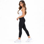 White side: Side view of white rhinestone knit slip-on sneakers worn with cropped black leggings.
