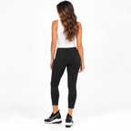 A woman shown from the back wearing black skinny jeans, a white tank top, and black sneakers with white soles, photographed against a clean white studio background.