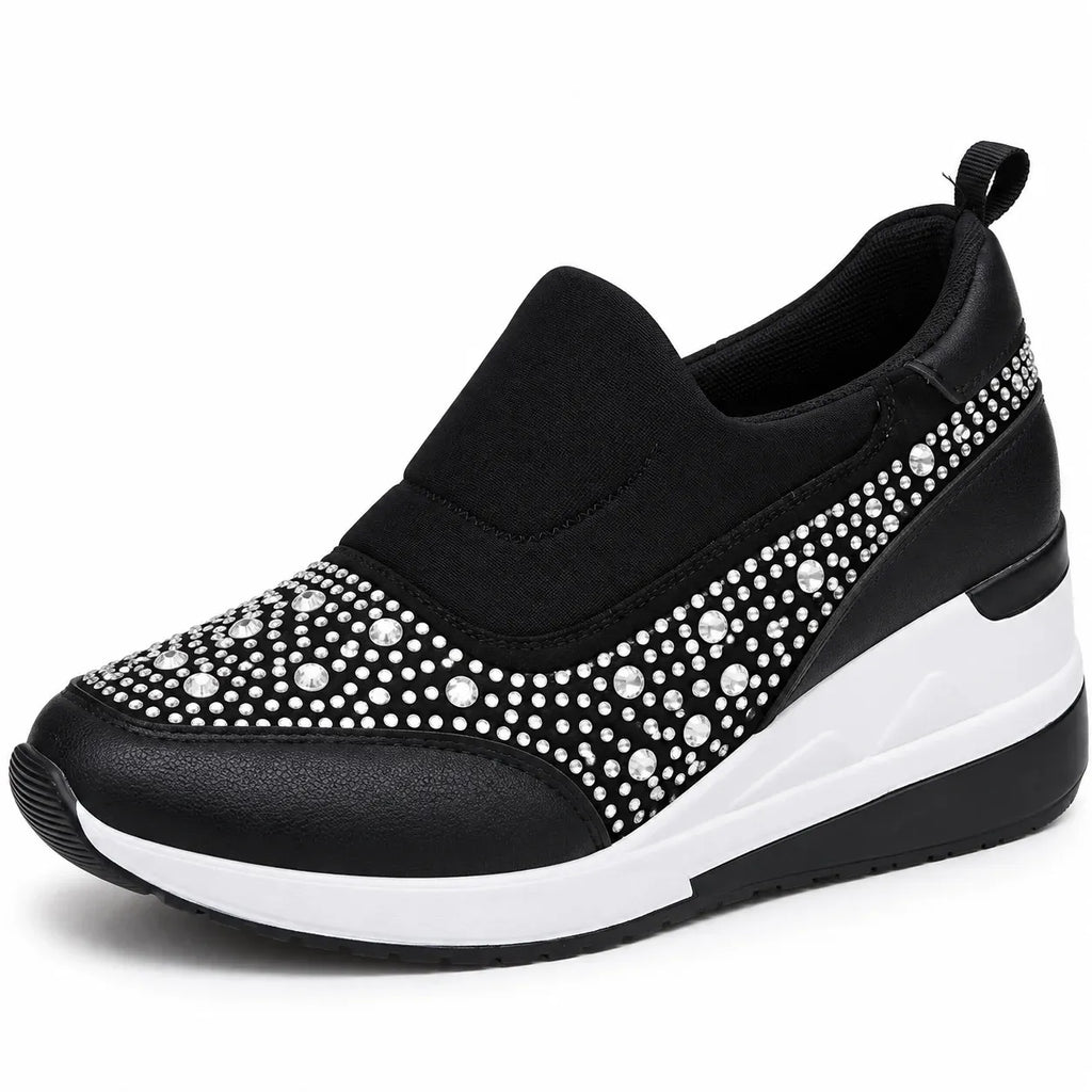 A black slip-on wedge sneaker decorated with silver rhinestones on the toe and side panels, featuring a thick white and black wedge sole.