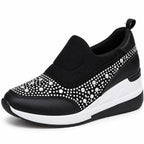 A black slip-on wedge sneaker decorated with silver rhinestones on the toe and side panels, featuring a thick white and black wedge sole.