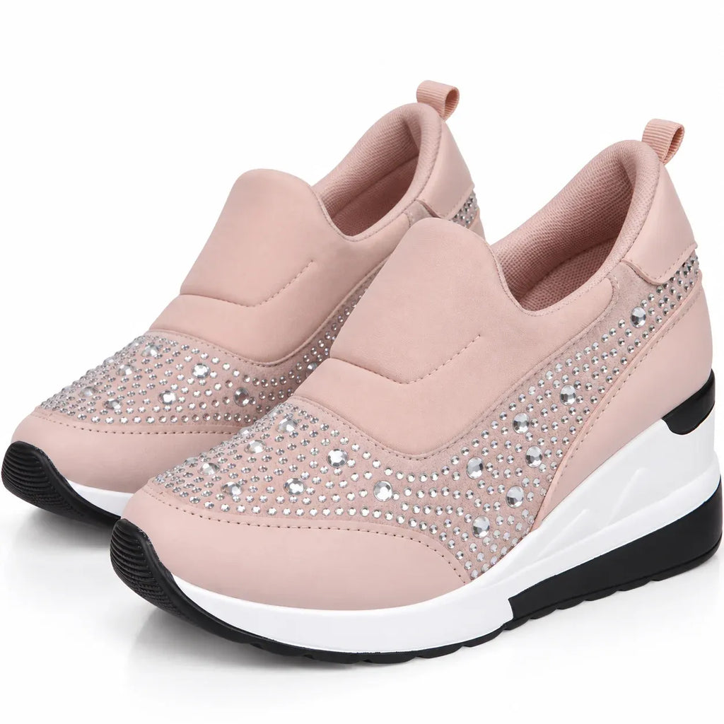 A pair of women's slip-on wedge sneakers in light pink, featuring silver rhinestone embellishments on the toe and side panels, with a white and black wedge sole.