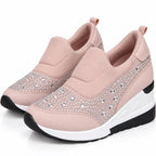 A pair of women's slip-on wedge sneakers in light pink, featuring silver rhinestone embellishments on the toe and side panels, with a white and black wedge sole.