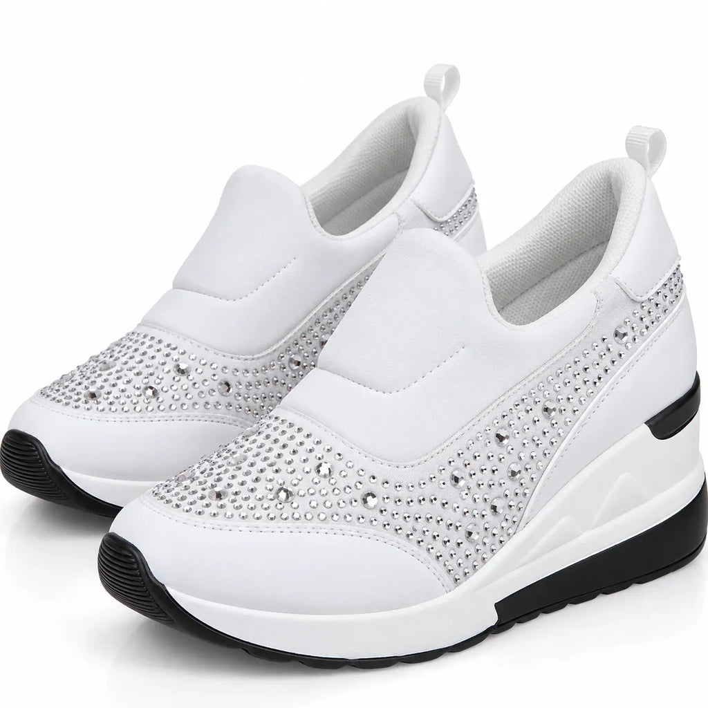 A pair of white slip-on wedge sneakers with silver rhinestone embellishments on the toe and side panels, featuring black outsole details, shown against a plain white background.