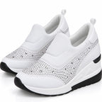 A pair of white slip-on wedge sneakers with silver rhinestone embellishments on the toe and side panels, featuring black outsole details, shown against a plain white background.