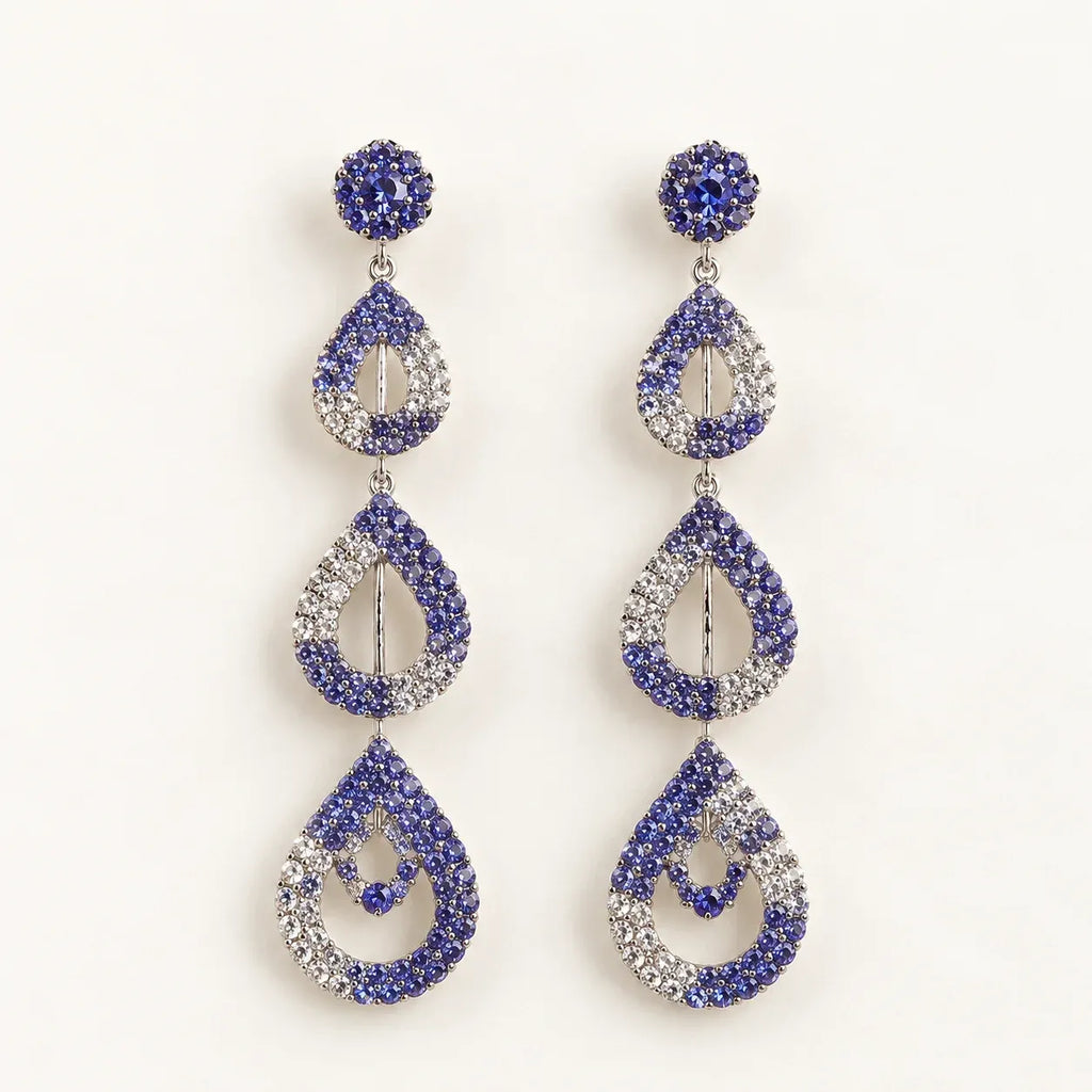 A pair of drop earrings with a silver-tone metal setting, featuring blue and clear rhinestones in a stacked teardrop design on a plain white background.
