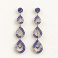 A pair of drop earrings with a silver-tone metal setting, featuring blue and clear rhinestones in a stacked teardrop design on a plain white background.
