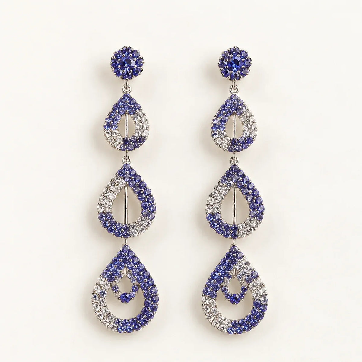 A pair of drop earrings with a silver-tone metal setting, featuring blue and clear rhinestones in a stacked teardrop design on a plain white background.
