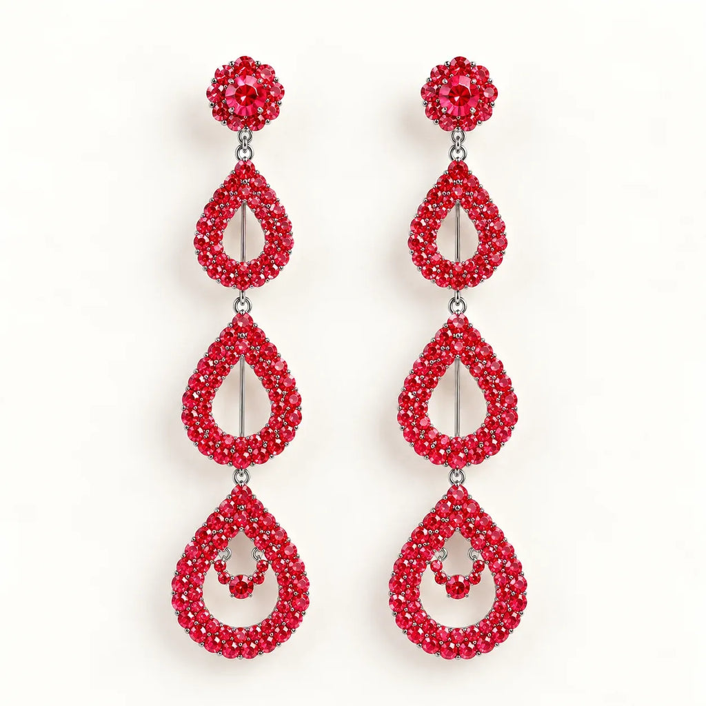 A pair of long drop earrings covered in sparkling red crystals, featuring a round stud at the top, a teardrop-shaped drop, and a larger teardrop drop with a small crystal accent in the center, set against a plain white background.