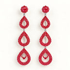 A pair of long drop earrings covered in sparkling red crystals, featuring a round stud at the top, a teardrop-shaped drop, and a larger teardrop drop with a small crystal accent in the center, set against a plain white background.