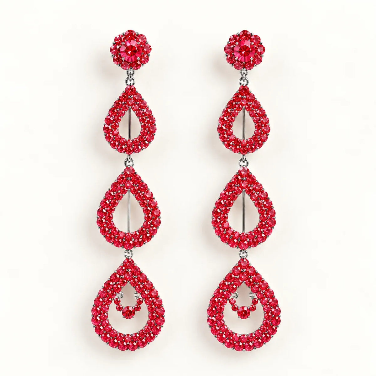 A pair of long drop earrings covered in sparkling red crystals, featuring a round stud at the top, a teardrop-shaped drop, and a larger teardrop drop with a small crystal accent in the center, set against a plain white background.