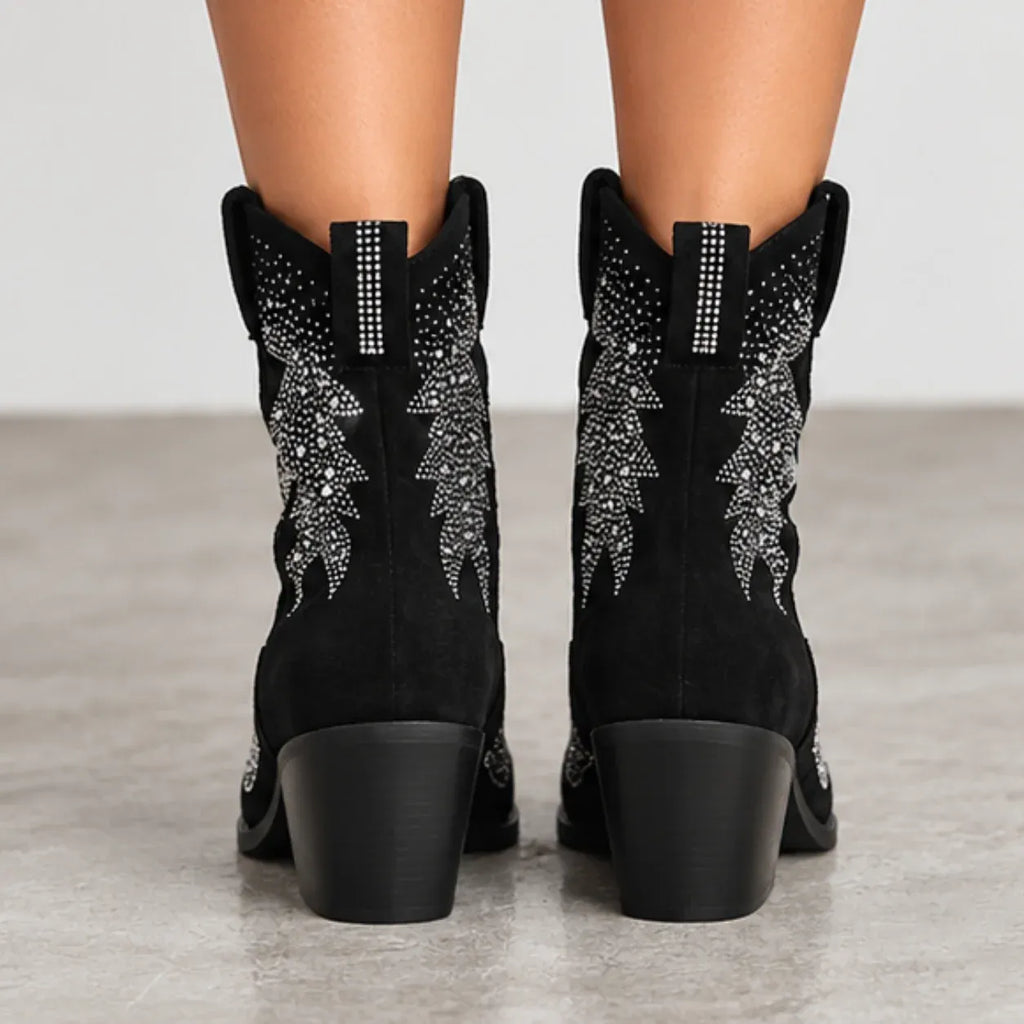Black suede cowboy boots with silver rhinestone embroidery on the shafts, shown from the back on a model's feet against a neutral gray background.