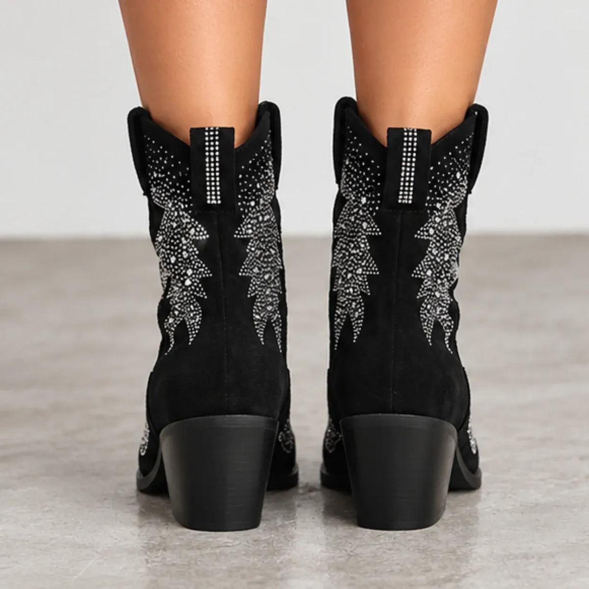 Black suede cowboy boots with silver rhinestone embroidery on the shafts, shown from the back on a model's feet against a neutral gray background.