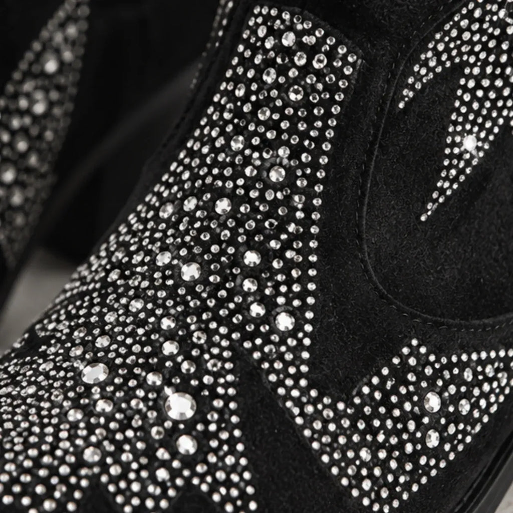 Close-up of a black suede boot covered with dense silver rhinestones and crystals, showing the textured shoe surface in high detail.
