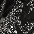 Close-up of a black suede boot covered with dense silver rhinestones and crystals, showing the textured shoe surface in high detail.